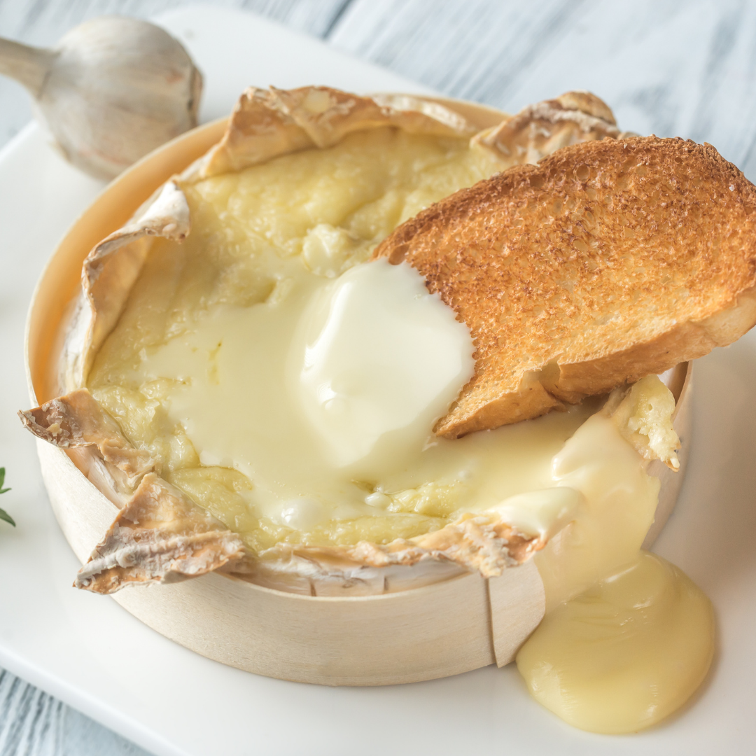 Baked Camembert in its wooden box with a slice of toast dipped into the melted cheese
