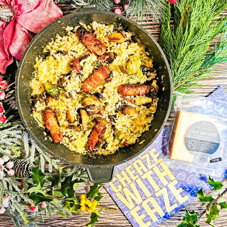 Brussels sprout risotto with pigs in blankets in a black pan, beside a 150g pack of Oak Smoked cheese and festive greenery