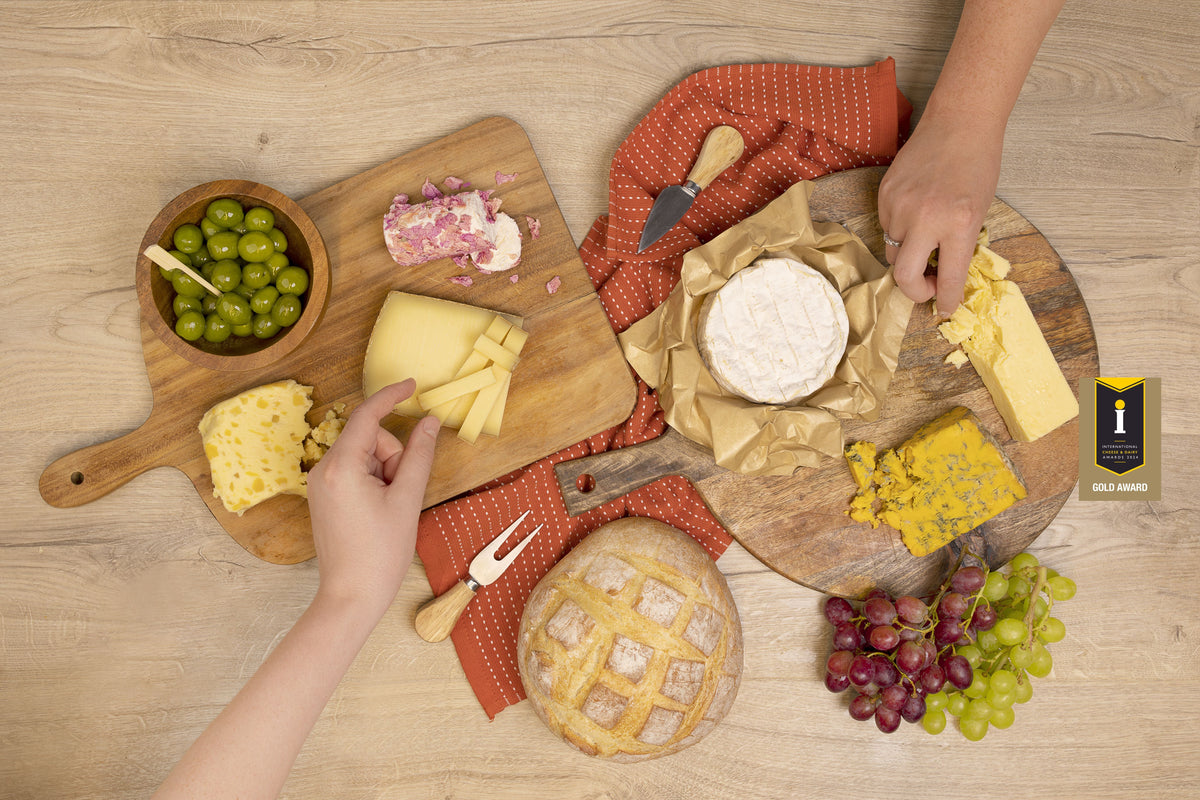 Hands reaching into a Cheese Box Club board of cheeses, olives, bread and grapes, with an ICDA 2024 Gold Award badge