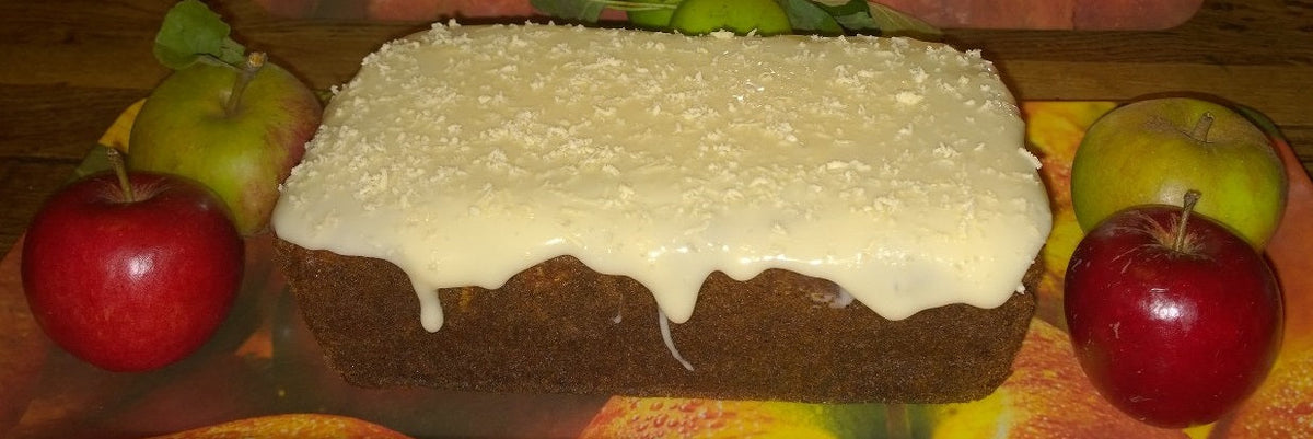Cheese and apple loaf cake with a thick white icing drizzle, surrounded by red and green apples