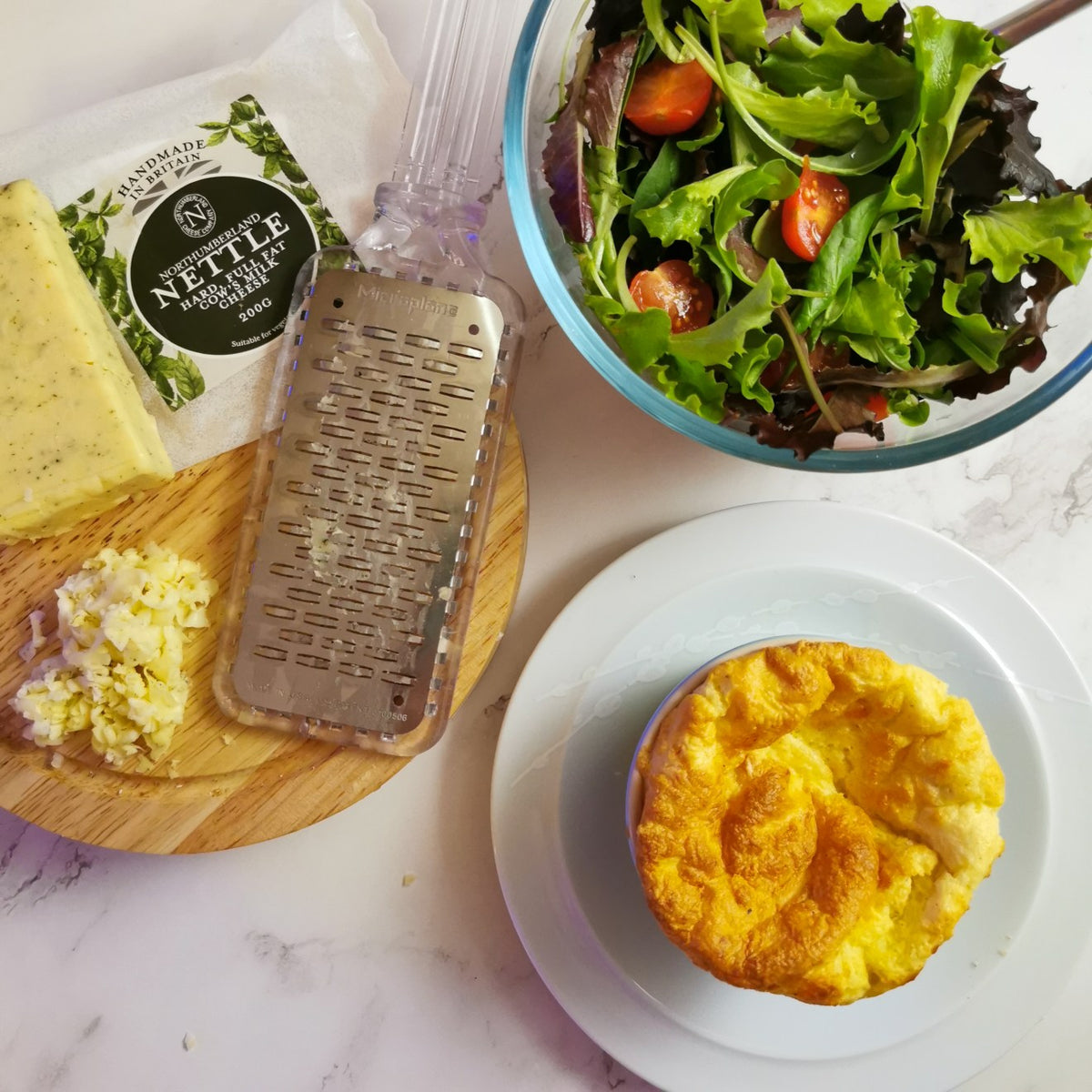 Nettle Cheese soufflé in a ramekin beside a 200g pack of Northumberland Nettle, grated cheese and a green salad