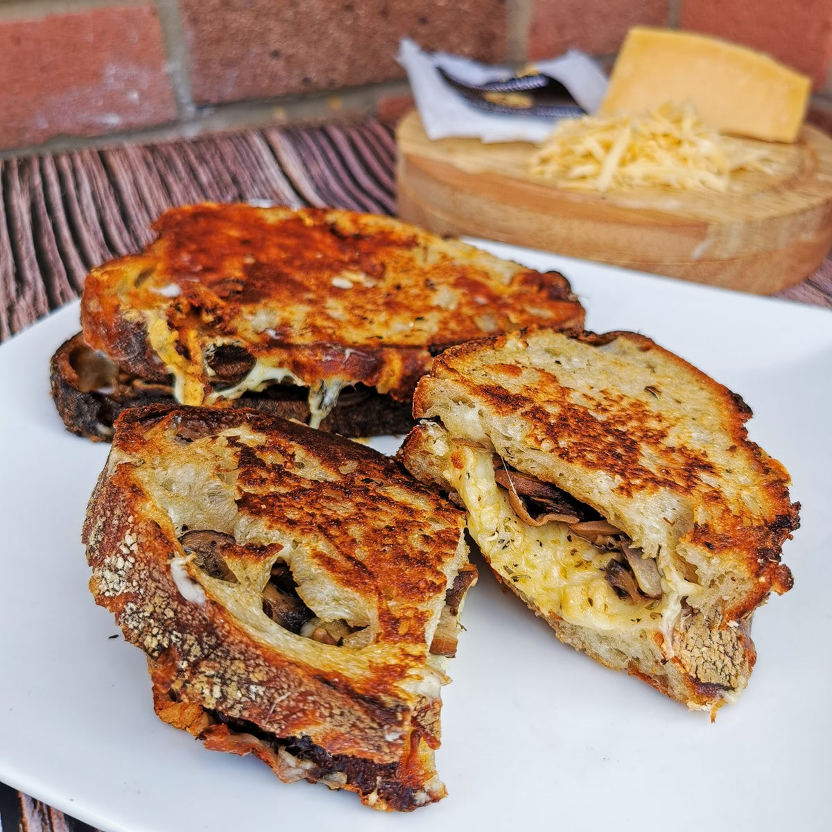 Mushroom and Gouda toasties cut open to show the melted cheese, with a wedge of Gouda and grated cheese behind