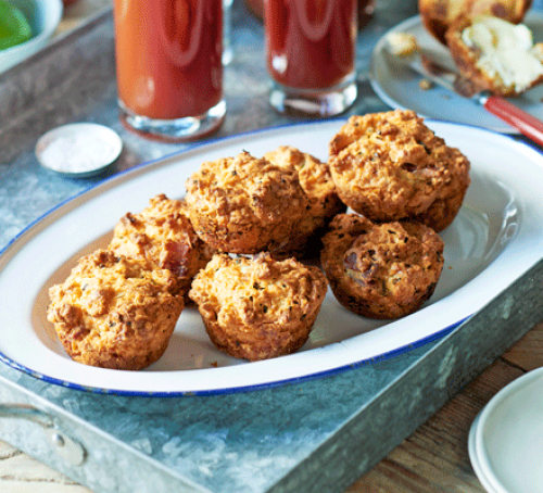 Cheese and bacon scones baked in muffin shapes on a blue-rimmed enamel platter, glasses of tomato juice behind