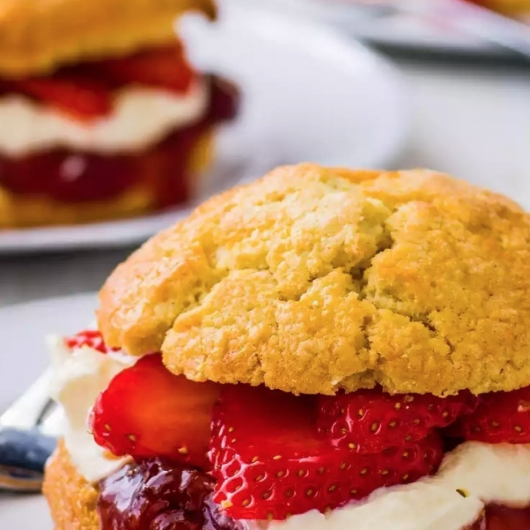 Golden scone split and filled with sliced strawberries, cream and jam, with a second filled scone behind