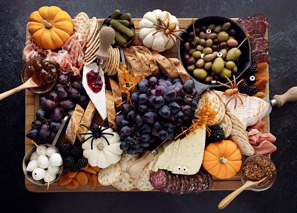 Halloween cheese board with cheeses, grapes, olives, crackers and cured meats, decorated with mini pumpkins and toy spiders