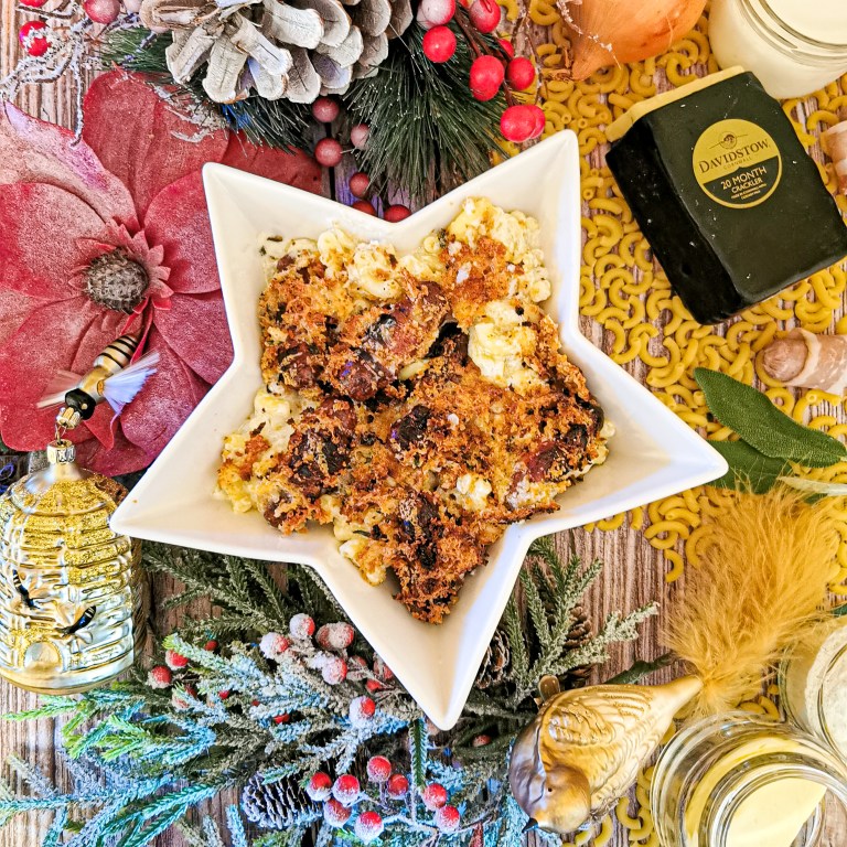 Star-shaped dish of macaroni cheese with pigs in blankets under a crisp crumb topping, among Christmas decorations