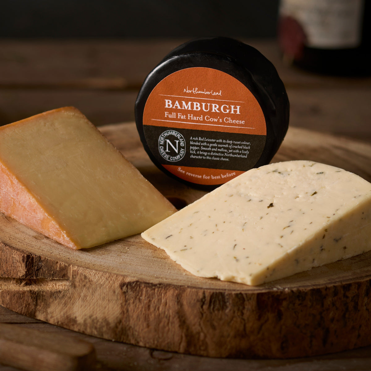A Bamburgh truckle in black wax between wedges of Oak Smoked and Nettle cheese on a log board