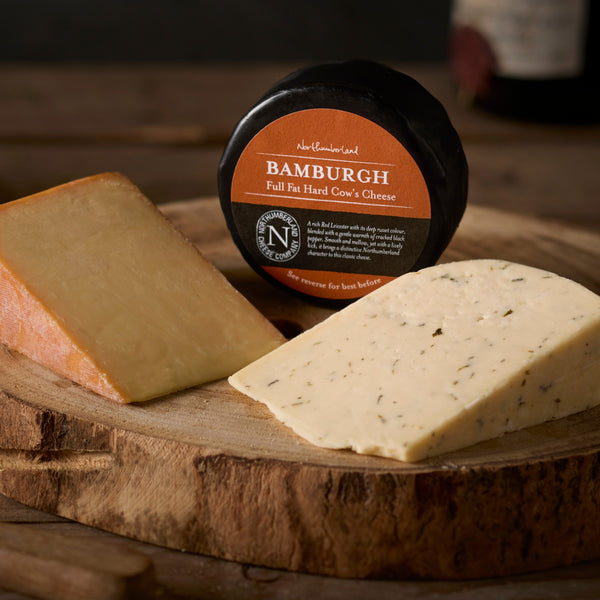 A Bamburgh truckle in black wax between wedges of Oak Smoked and Nettle cheese on a log board