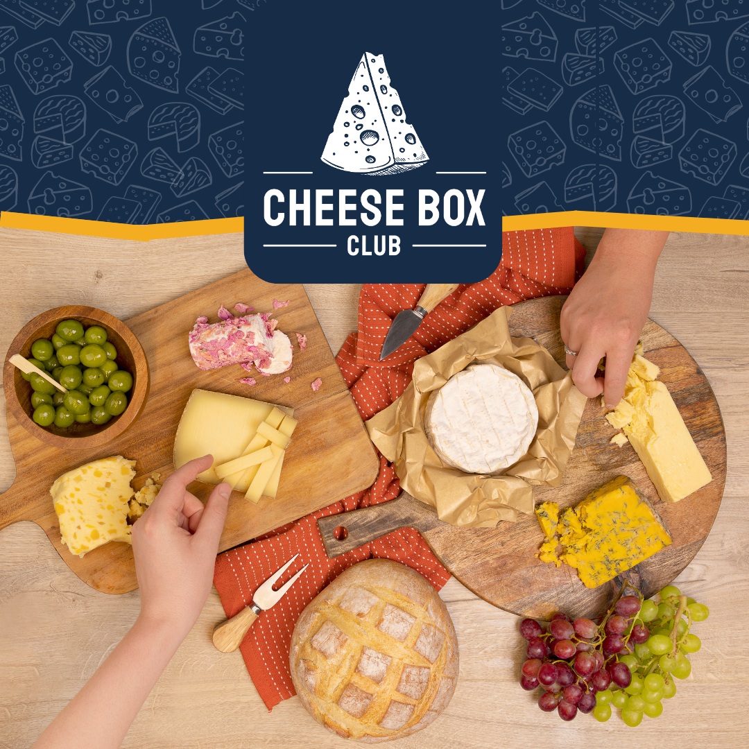 Hands reaching into a spread of cheeses, olives, grapes and a crusty loaf under the Cheese Box Club logo