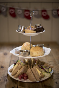 Cheese Loft Café afternoon tea stand with cheese sandwiches, scones and cakes, festive stocking bunting behind