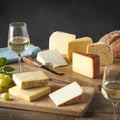 Cheesed Off Cheese Board selection of eight cheeses laid out on wooden boards with white wine, green grapes and bread
