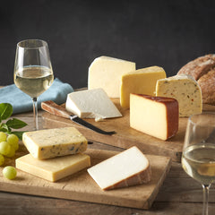 Cheesed Off Cheese Board selection of eight cheeses laid out on wooden boards with white wine, green grapes and bread