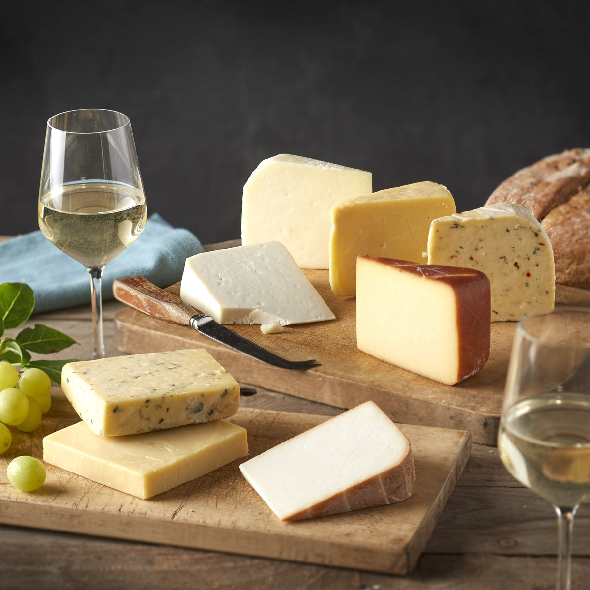 Cheesed Off Cheese Board selection of eight cheeses laid out on wooden boards with white wine, green grapes and bread