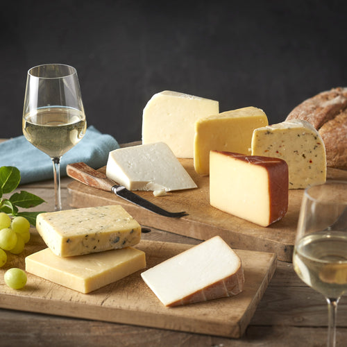 Cheesed Off Cheese Board selection of eight cheeses laid out on wooden boards with white wine, green grapes and bread