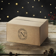 Brown cardboard box stamped with the Northumberland Cheese Company logo, on a wooden table with fairy lights and pine cones