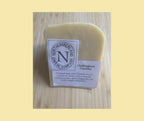 Chillingham Cheddar wedge on a light wooden board, with its plain white Northumberland Cheese Company labels