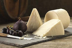 Wedges and a small round of white Elsdon goats' cheese on a slate with a fresh fig, black grapes and a cheese knife