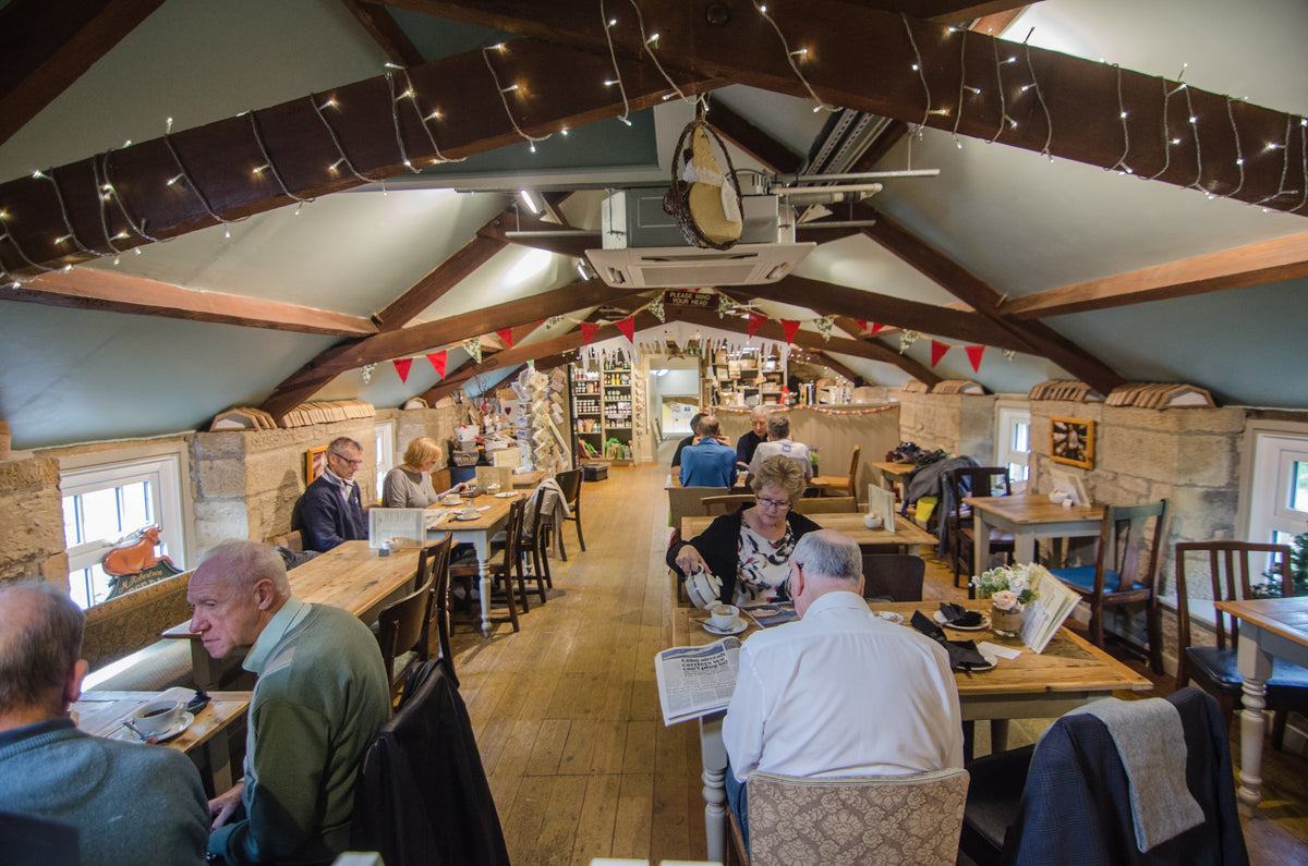 Inside the Cheese Loft Cafe: beamed ceiling with fairy lights, bunting and customers at wooden tables