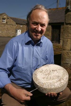 Founder Marc Robertson holding a whole truckle of Northumberland cheese in the farmyard