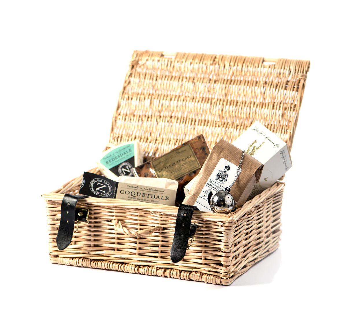 An open wicker gift hamper holding Redesdale and Coquetdale cheeses, a rich fruit cake and tea with a tea infuser