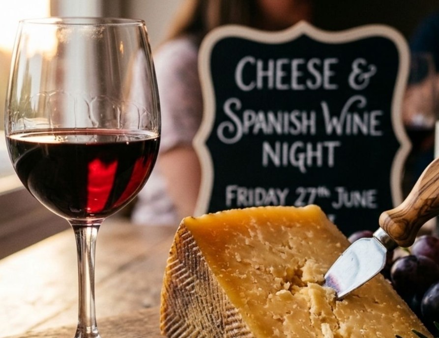 A glass of red wine and a wedge of hard cheese in front of a chalkboard for a Cheese & Spanish Wine Night