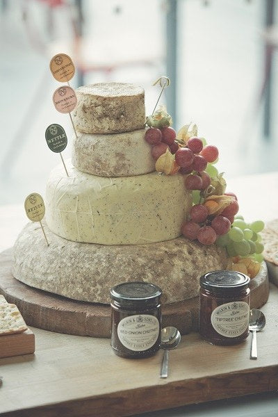 Four-tier cheese wedding cake with a flag naming each cheese, red and green grapes, and two jars of chutney in front