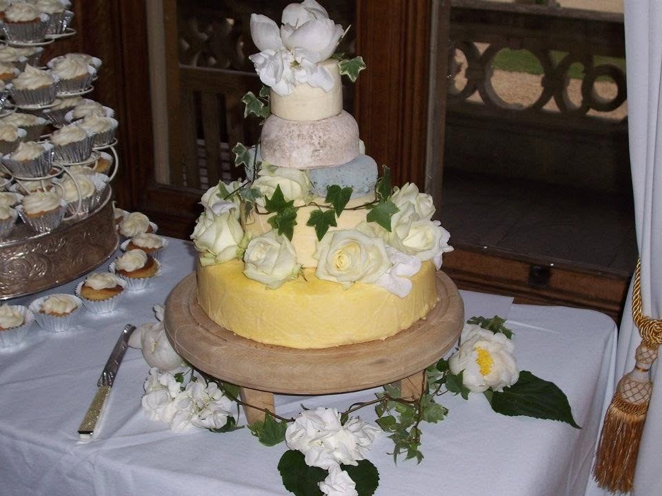 Cheese wedding cake decorated with white roses and trailing ivy on a wooden stand, with a tower of cupcakes beside it