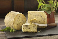Nettle Cheese truckle and wedges flecked with nettles on a slate, with fresh nettle leaves and a cheese knife