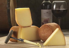 Oak Smoked Cheese truckles with bronzed rinds and pale wedges, a cheese iron, and a bottle and glass of red wine