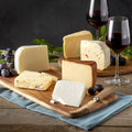 Taste of Northumberland cheeses cut into wedges on wooden boards with red wine, black grapes and a knife