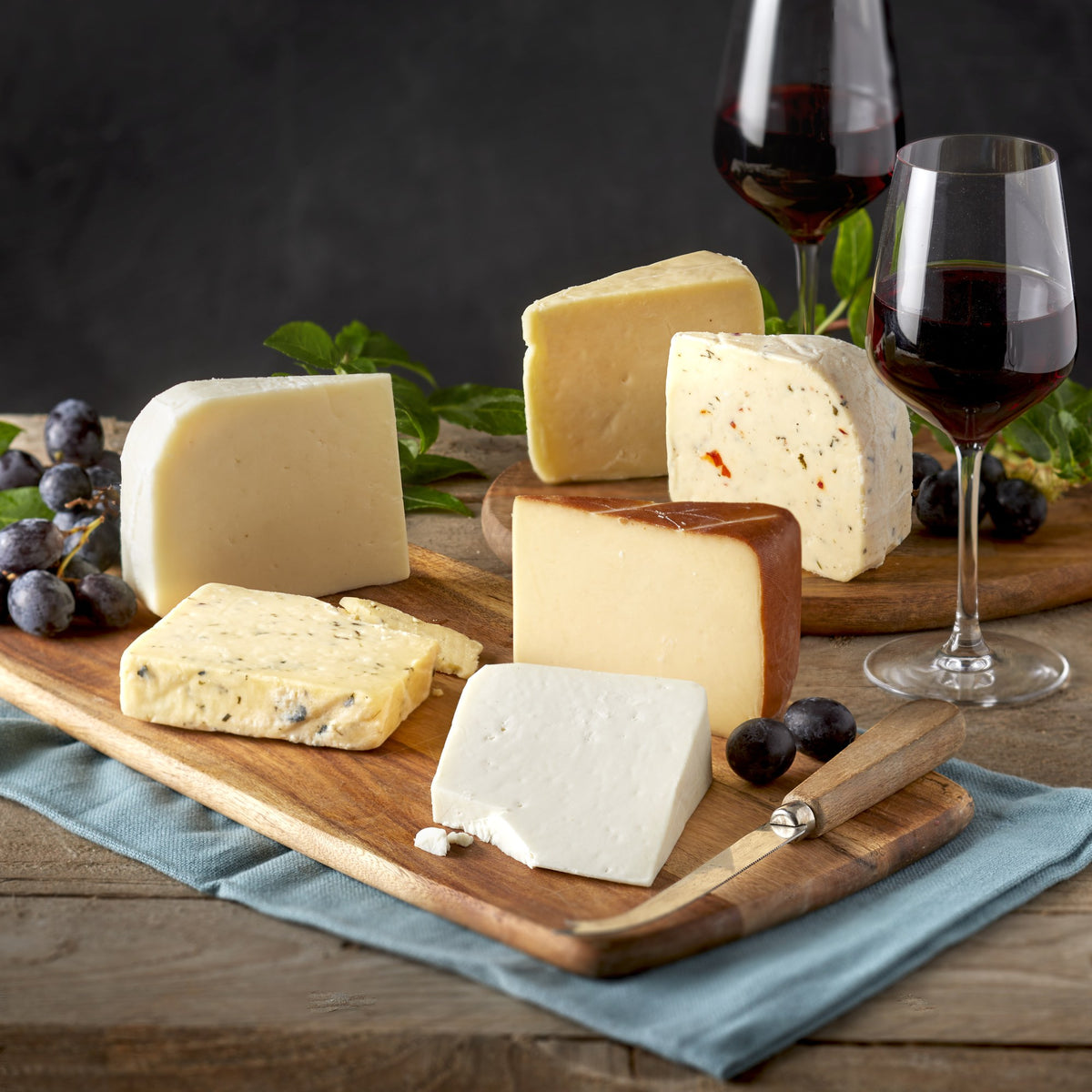 Taste of Northumberland cheeses cut into wedges on wooden boards with red wine, black grapes and a knife