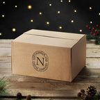 Brown box for the Twelve Cheeses of Christmas Box, stamped with the Northumberland Cheese Company logo, among fairy lights and pine cones