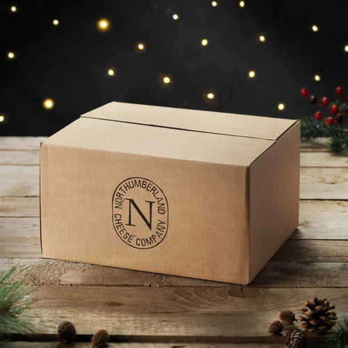 Brown box for the Twelve Cheeses of Christmas Box, stamped with the Northumberland Cheese Company logo, among fairy lights and pine cones