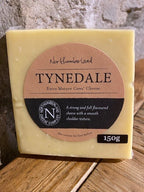 Vacuum-packed 150g block of Tynedale Extra Mature with a weight sticker, propped on a wooden shelf against a stone wall